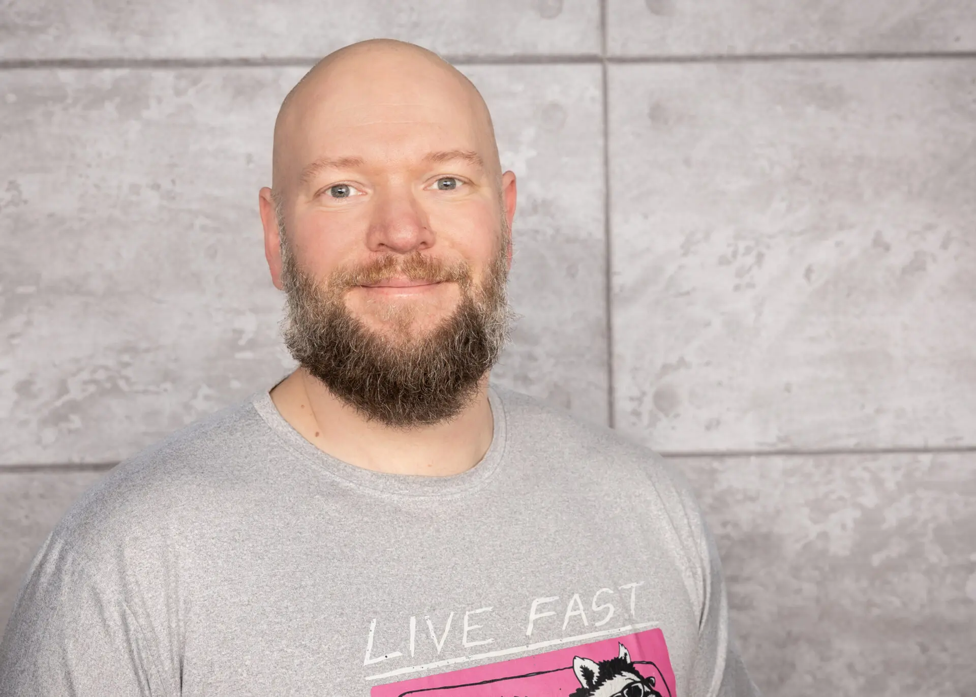 Stefan Fernahl mit kurzem, glattem Kopf und Bart, trägt ein graues T-Shirt mit dem Aufdruck 'LIVE FAST'.